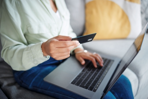 Fata care sta cu laptopul pe picioare și cu cardul în mână pentru a plasa o comandă online