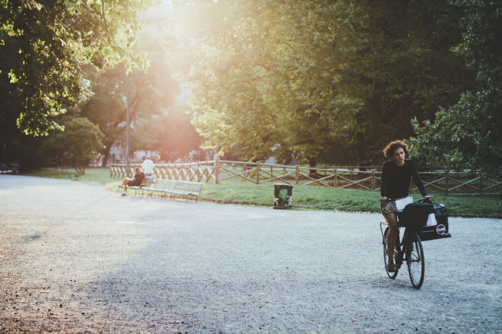 O a unei fete ce se plimba cu bicicleta poza intr-un parc plin de copaci verzi